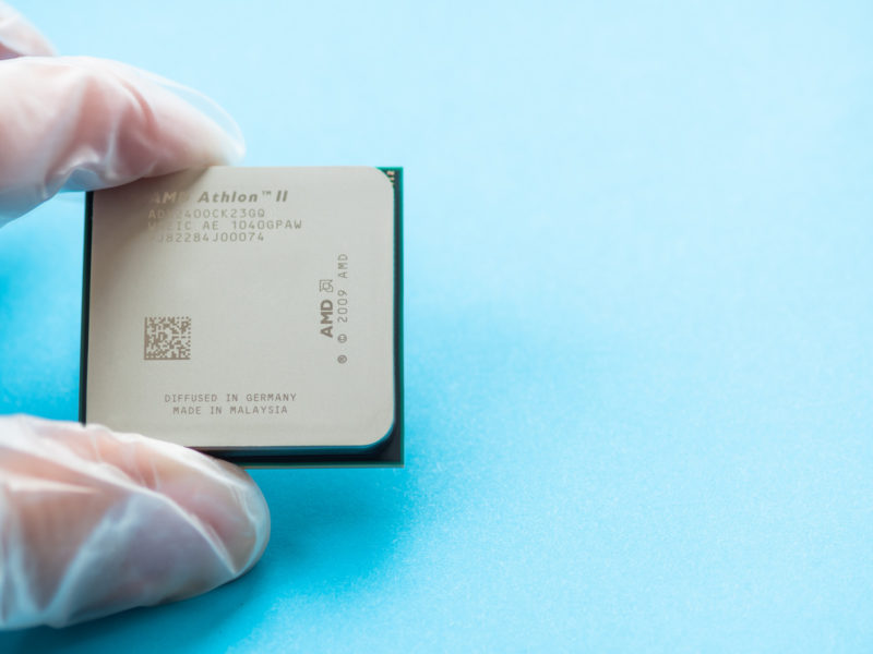 MOSCOW, RUSSIA - October 11, 2019. Hand in rubber glove with AMD Athlon II Central Computer Processor. CPU on blue background. Technological detail of personal computer.