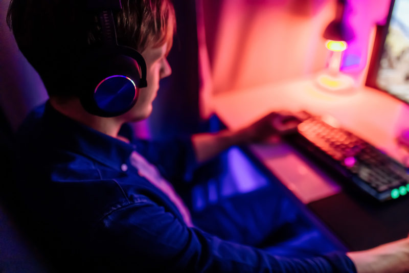 professional gamer playing computer games online with headphones, in a room with neon light.